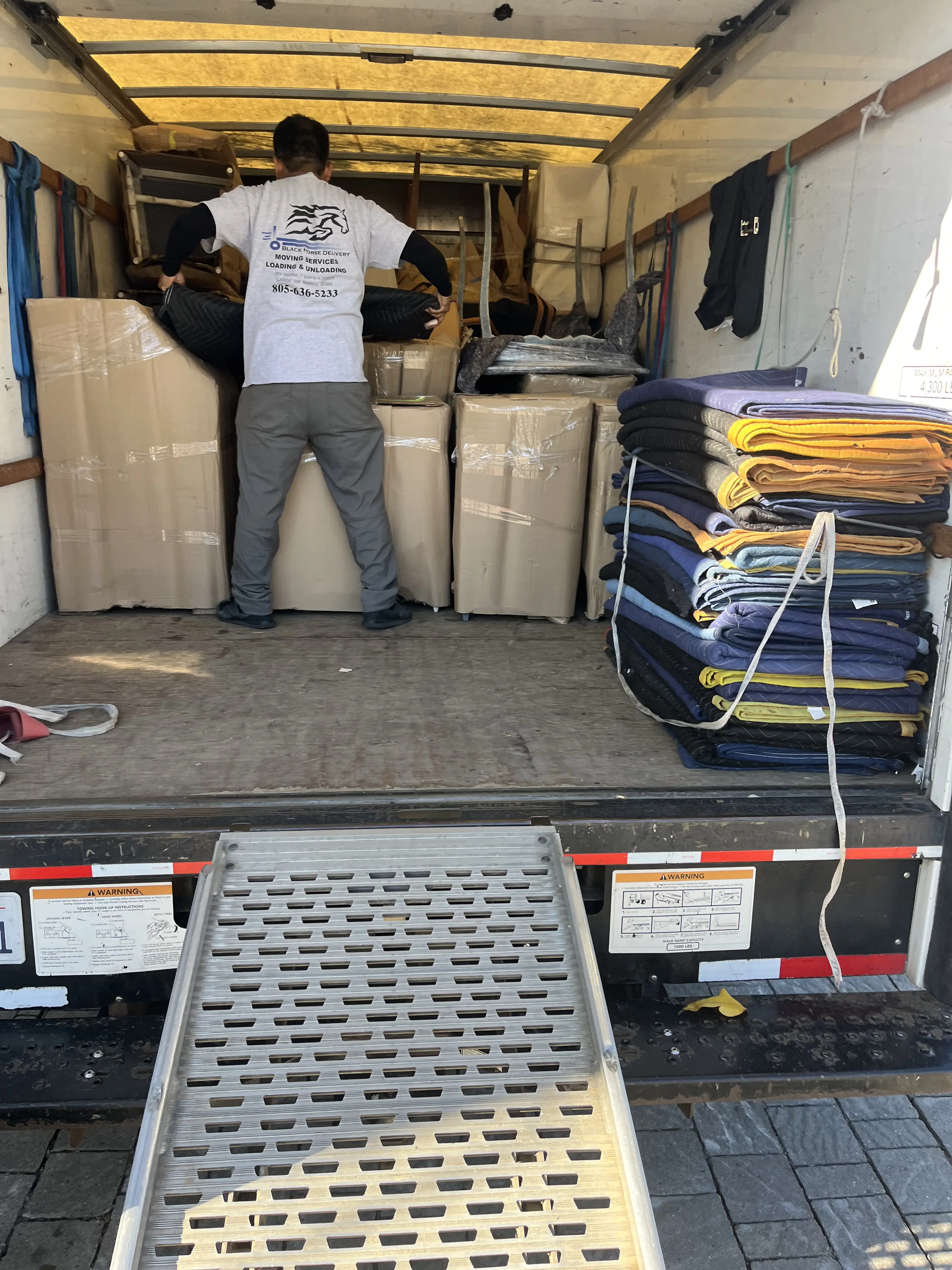 Black Horse Delivery mover organizing items inside a moving truck with ramp extended